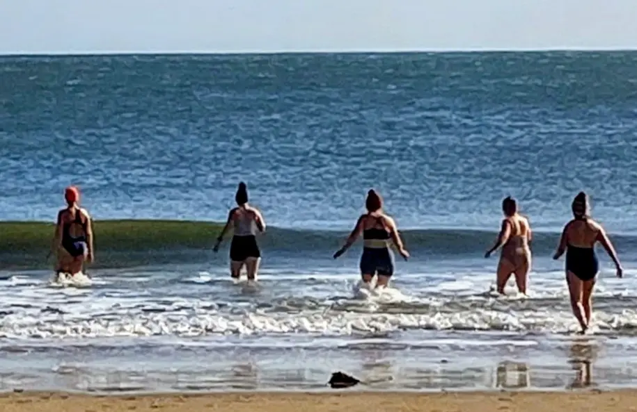 A group walking together into the sea at Embleton Bay